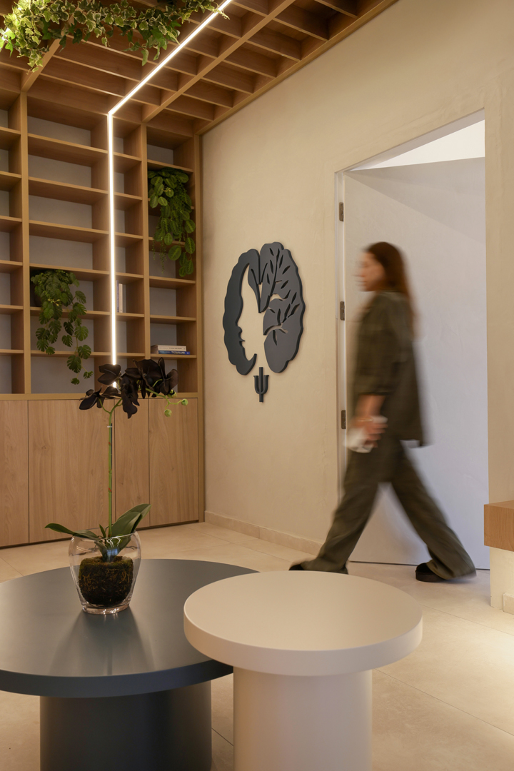 Psychologist office interior by KK Interior Design with shelving wall, integrated vertical lighting, decorative plants, and wall-mounted emblem