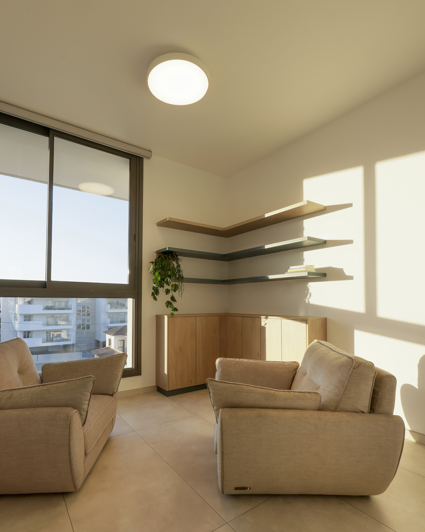 Private therapy room interior by KK Interior Design featuring armchairs, floating shelves, indoor plants, and large window with city view