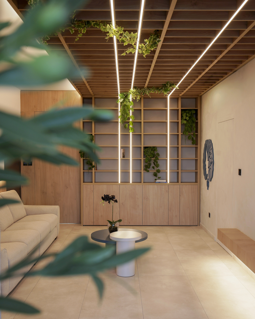 Interior view through terrace opening by KK Interior Design showing ceiling grid lighting, shelving wall, and calm waiting area composition
