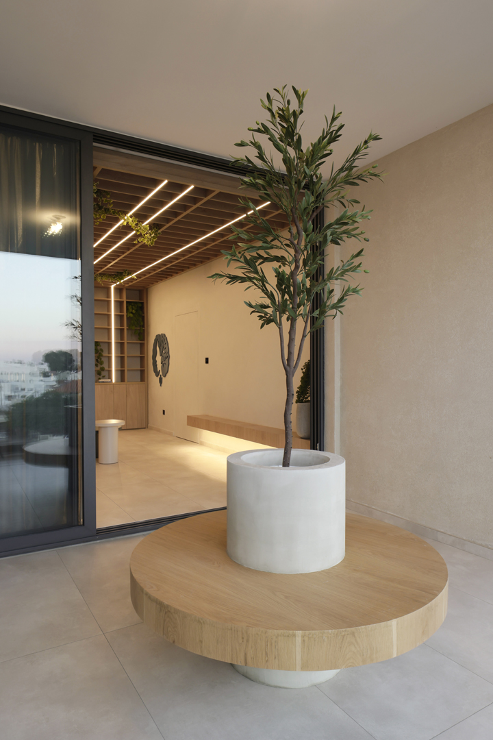Psychologist office interior framed by foreground greenery by KK Interior Design highlighting shelving wall, integrated lighting, and seating area