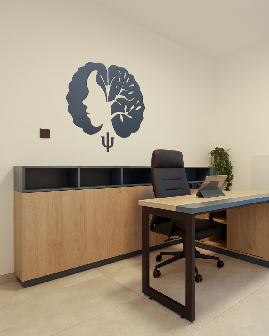 Psychologist office consultation workspace by KK Interior Design with desk, executive chair, storage cabinetry, and wall-mounted emblem
