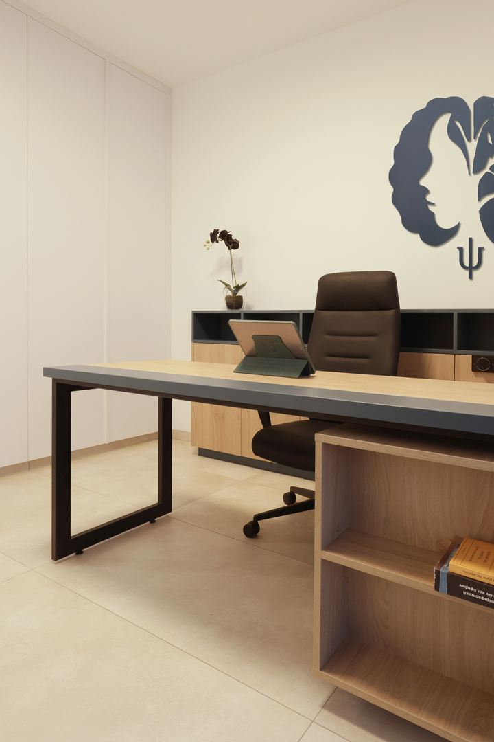 Detail view of psychologist office desk by KK Interior Design showing wood surfaces, integrated storage, books, and minimalist furnishings