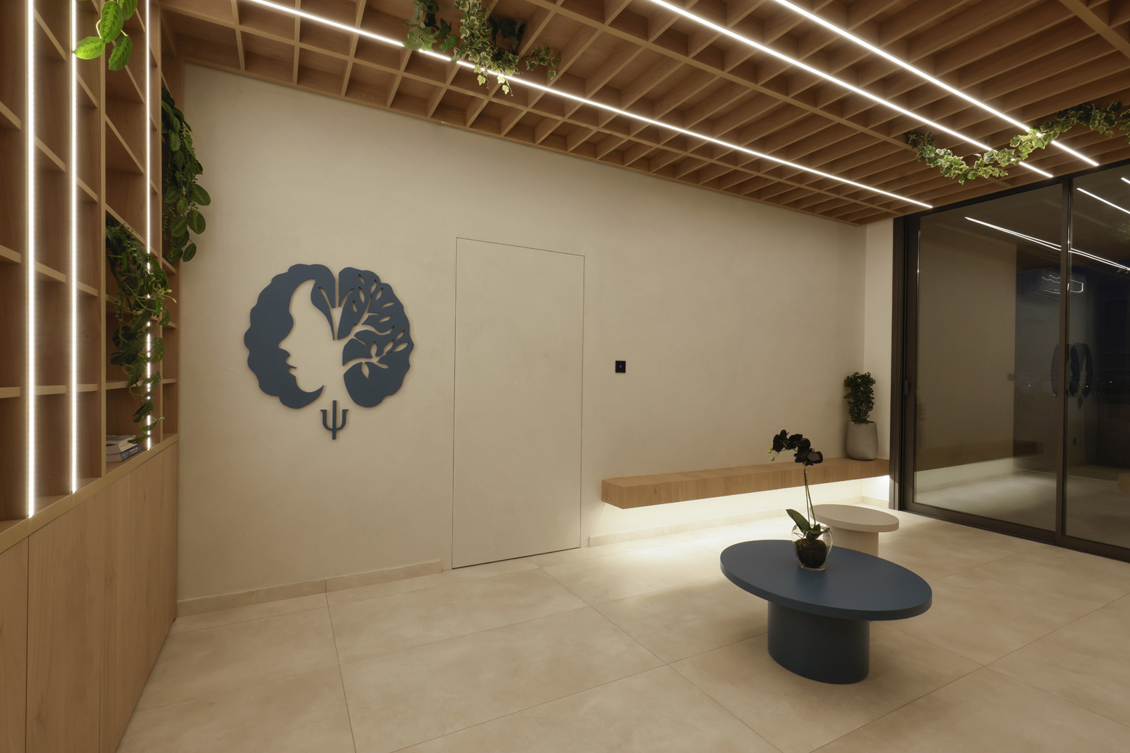Psychologist office waiting area by KK Interior Design with wall emblem, floating bench, coffee table, and ceiling grid with linear lighting
