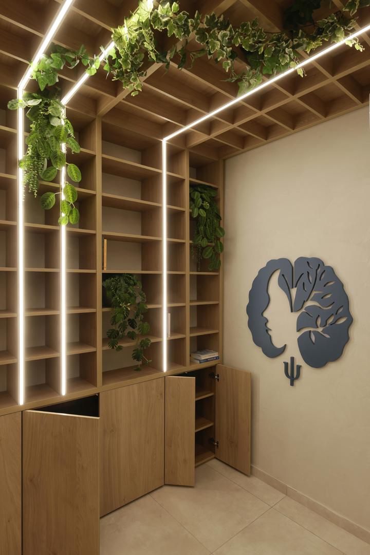 Open storage detail of psychologist office shelving by KK Interior Design showing illuminated shelves, plants, and cabinetry doors