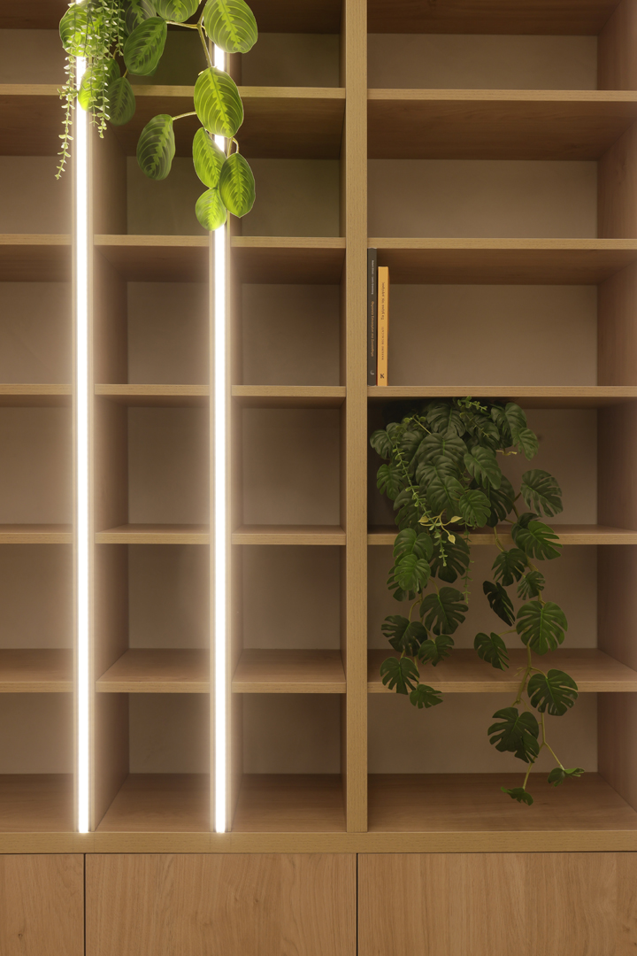 Detail of psychologist office shelving by KK Interior Design with vertical LED lighting, indoor plants, and wood finishes